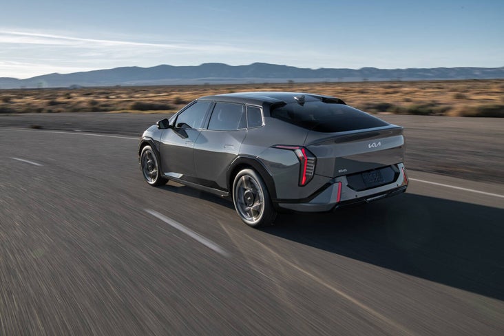 Rear three-quarter view of a dark gray Kia EV6 GT driving fast on a desert highway with blurred motion.