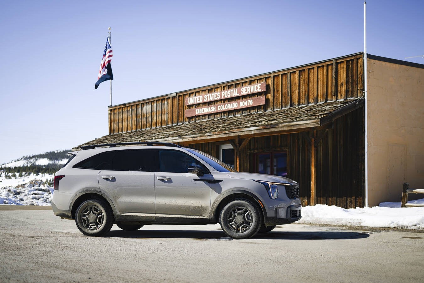 A grey American Made 2026 Kia Sorento in Phoenix is parked facing right in front of the old wooden United States Post Office in Tabernash, Colorado with snow in the background.