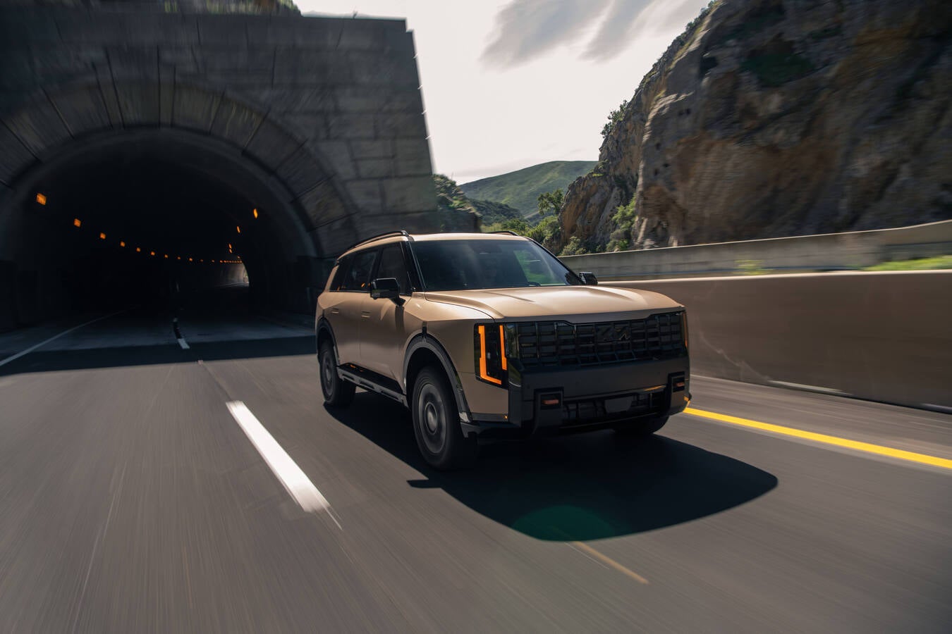 A brown 2027 Kia Telluride in Phoenix drives towards the viewer to the right ona road exiting a tunnel.
